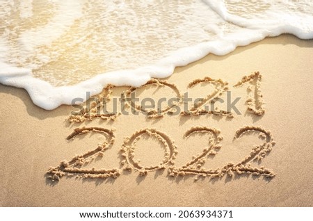 End of 2021 Happy New Year 2022, lettering on sunrise beach with wave and foam bubble in the morning. Handwritten inscription 2021 and 2022 on beautiful sand beach. New Year 2022 replace 2021 concept.