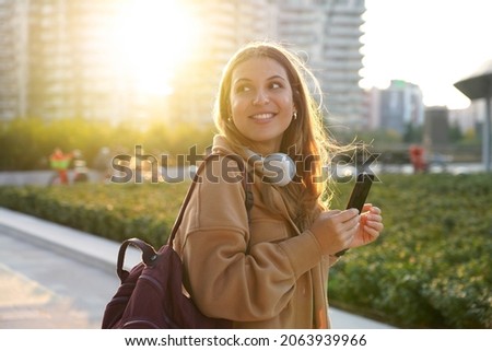 Sunshine girl with coat and backpack turn around and looks to the side on modern city street at sunset Royalty-Free Stock Photo #2063939966