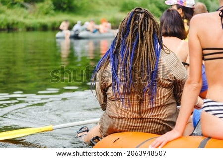 A very fat man, presumably a woman, with a haircut with dreadlocks, is rafting down the river as part of a group of young people. Royalty-Free Stock Photo #2063948507