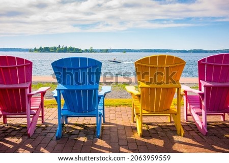 Four painted Adirondack chairs lined up along the bank of the St. Lawrence River in Clayton, New York.  Royalty-Free Stock Photo #2063959559