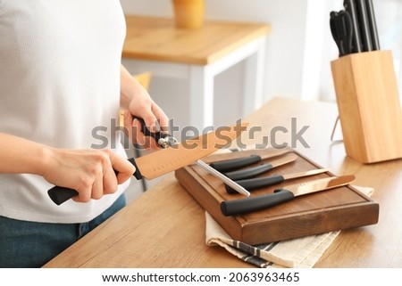 Woman sharpening knife in kitchen, closeup Royalty-Free Stock Photo #2063963465