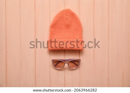 Stylish warm hat and sunglasses on color wooden background