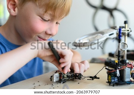 Young smiling inventor kid carefully assembling robotic toy with screwdriver, working with small mechanical parts, using magnifier glass. STEM Education Royalty-Free Stock Photo #2063979707