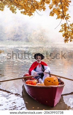 young man dressed as gondolier in gondola boat decorated with pumpkins on pond in autumn park celebrates Halloween and having fun, concept of Halloween carnival or costume party