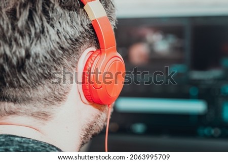 Freelancer wearing headphones editing video using postproduction software while working at home.Videographer processes the film movie editing.Selective focus,back view, copy space.Cinema toned.