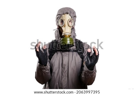 An isolated shot of a man dressed in a gas mask, a jacket with a hood, a backpack, holding his hands in front of him as if there was something in them, looking into the camera. On a white isolated Royalty-Free Stock Photo #2063997395