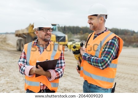 Two professional road construction workers in orange vests and protective helmets in the middle on the terrain Royalty-Free Stock Photo #2064009020