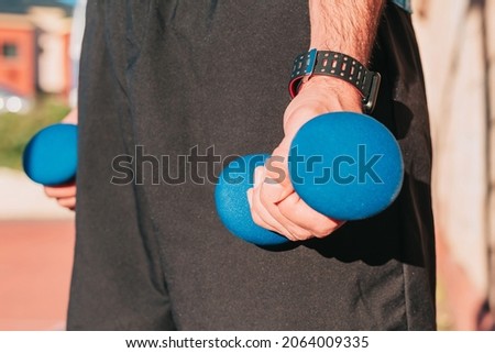Close up shot of the hands of a sportsman holding weights with a smart whatch on his wrist while training outdoors. Sports and gym equipment concept.