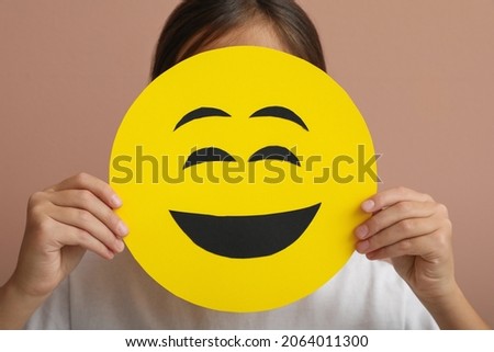 Little girl covering face with laughing emoji on pale pink background