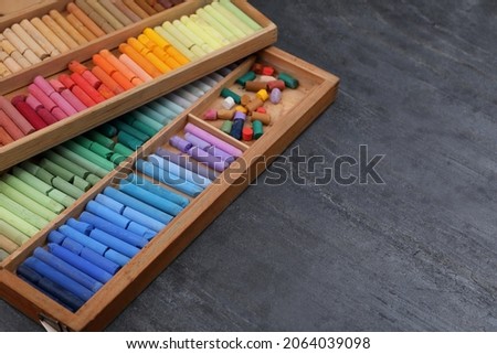 Colorful pastels in wooden trays on grey stone table, space for text. Drawing materials