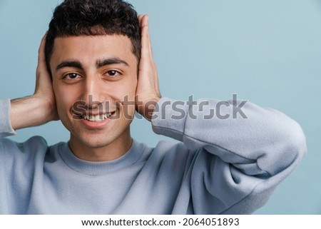 Young middle eastern man smiling and covering his ears isolated over blue background