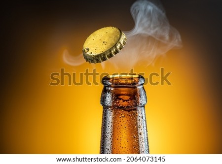 Opening of cold beer bottle - gas output and bottle cap in the air. Isolated on a yellow background. Royalty-Free Stock Photo #2064073145