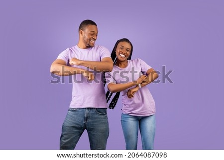 Having Fun. Portarit of happy positive young black couple dancing and fooling around. Cheerful African American guy and lady with long braids enjoying favorite music together, violet studio background
