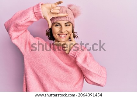 Young brunette woman wearing cute wool cap smiling making frame with hands and fingers with happy face. creativity and photography concept. 