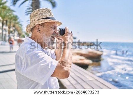 Senior man smiling confident wearing summer hat using camera at seaside