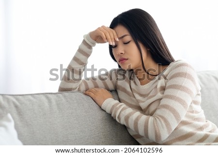 Depression Concept. Young Upset Asian Woman Sitting On Sofa At Home, Depressed Korean Female Feeling Sad And Lonely, Leaning Head On Hand While Resting On Couch In Living Room, Free Space Royalty-Free Stock Photo #2064102596