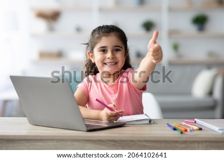 Distant Learning. Little Arab Girl Showing Thumb Up While Study With Laptop At Home, Smiling Female Child Sitting At Table With Computer In Living Room, Recommending Online Education, Copy Space Royalty-Free Stock Photo #2064102641