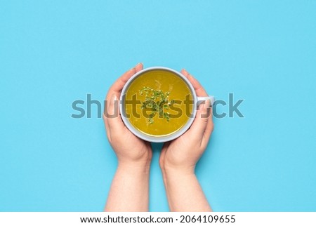 Woman hands holding a mug with hot chicken soup over a blue background. Delicious and healthy homemade broth.