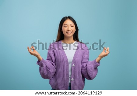 Zen. Peaceful asian lady meditating with closed eyes, practicing yoga and keeping hands in mudra gesture, standing isolated over blue background, free space