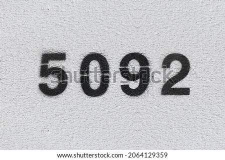 Black Number 5092 on the white wall. Spray paint. Number five thousand ninety two.