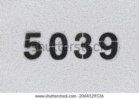 Black Number 5039 on the white wall. Spray paint. Number five thousand thirty nine.