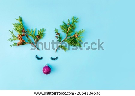The reindeer Christmas face is made of Christmas tree twigs, eyelashes and pink decorations. On a pastel blue background. Creative New Year's composition. Copy space.