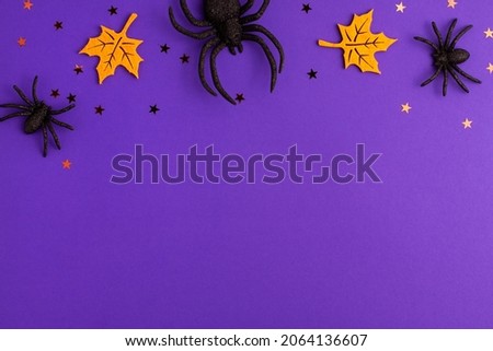 One big and two tiny black artificial spiders stars and yellow felt leaves on purple background with copy space. Halloween scary holiday and autumn concept