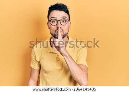 Young hispanic man wearing casual clothes and glasses asking to be quiet with finger on lips. silence and secret concept. 
