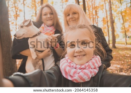 Mother, grandmother and little granddaughter with jack russell terrier dog taking selfie by smartphone outdoors in autumn nature. Family, pets and generation concept