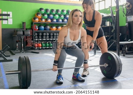 Female coach correcting a concentrated young girl who is going to lift some weights in a gym.Selective focus