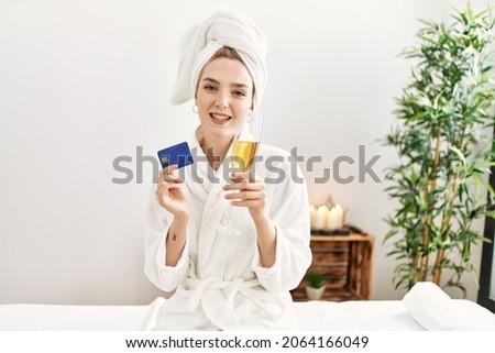 Young caucasian woman relaxed drinking champagne holding credit card at beauty center.