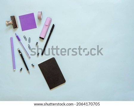 Flat lay of purple stationery on blue background with copy space. Top view of office supplies for writer and brainstorming. Top view of blank sticky note with pencils and a small notebook.