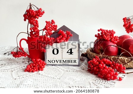 Calendar for November 4: the name of the month in English, the numbers 0 and 4, a bouquet of viburnum and viburnum branches, apples on a tray on a gray openwork napkin, gray background