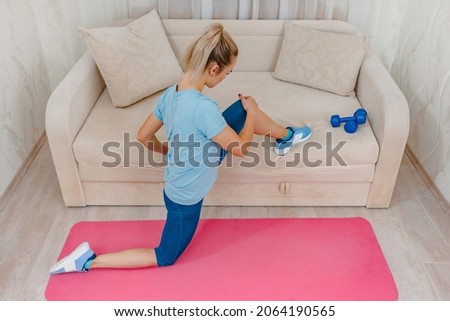 Sporty fit young woman using sofa for stretching legs,