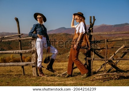 Outdoor full-length fashion portrait of two confident women wearing stylish outfits, posing in autumn mountains. Copy, empty space for text Royalty-Free Stock Photo #2064216239