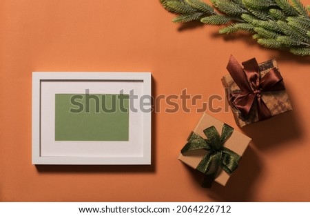 White frame with green background for the inscription. Branches with green needles are decorated with a red star. Two gift boxes are decorated with bows. Christmas background.