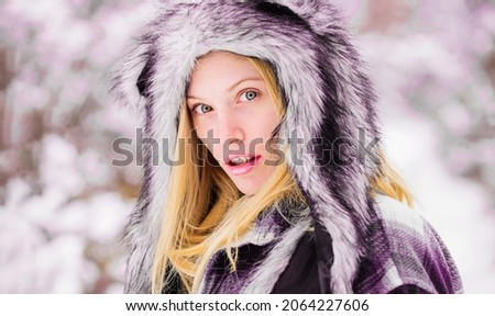 Wintertime. Closeup portrait girl in snow park. Beautiful young woman in warm coat and fur hat. Season of winter.