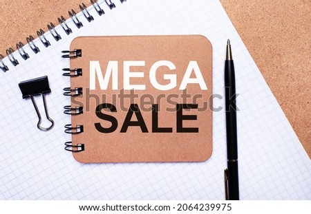 On a wooden background notepad, black pen, paper clip and brown notepad with the text MEGA SALE. Business concept