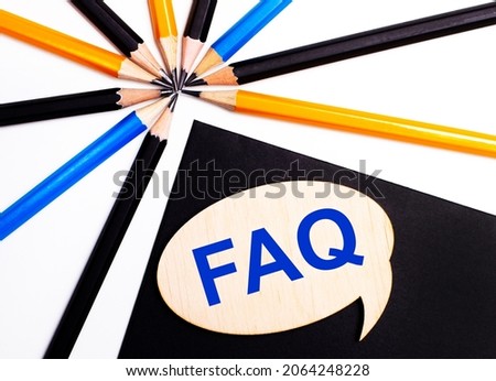 Wooden card with the text FAQ on a black background near multicolored pencils.