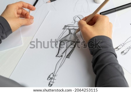 Clothing designer draws sketches on paper in the workplace. The artist creates a model for the dress. Fashion concept.