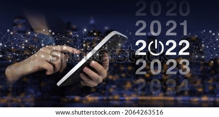 New year concept. Hand touch white tablet with digital hologram 2022 sign on city dark blurred background. 2022 new year. Concept Start New Year 2022