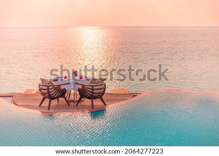 Seascape view under sunset light with dining table with infinity pool around. Romantic tropical getaway for two, couple concept. Chairs, food and romance. Luxury destination dining, honeymoon template Royalty-Free Stock Photo #2064277223