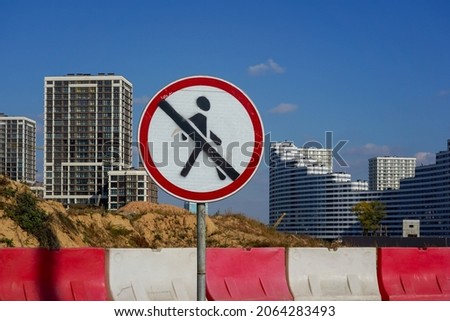 Photo of a round white-red road sign with a crossed out man on the background of a construction of multi-storey buildings in the city.