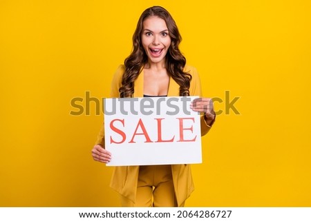 Photo of excited funny young lady wear suit jacket holding sale card smiling isolated yellow color background