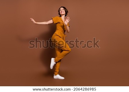 Full length photo of cheerful positive cool young woman dance wear look empty space isolated on brown color background