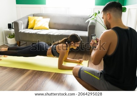 Rear view of a young man taking a picture with a phone of his fitness sporty girlfriend doing a plank exercises 
