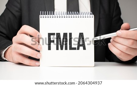 man writes in a notebook with a silver pen and hand holding card with text fmla. grey background, front view. business and education concept.