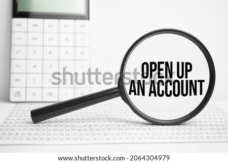 Magnifying glass with text OPEN UP AN ACCOUNT on white table with calculator