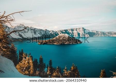 The blue crater lake with an island in the middle surrounded by low snowy mountains in the background HD Wallpaper Nature Adventure Beauty natural Hills and Mountains