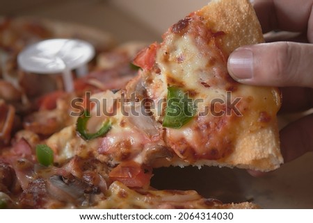 Man's hand holding a pizza slice out of the box closeup